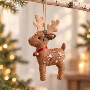 May include: A brown felt reindeer ornament featuring light tan antlers, a red ribbon collar with a small gold bell, and green holly leaves with red berries. The body is decorated with white and red embroidered snowflake patterns.