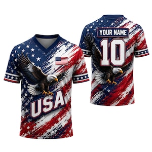 Può includere: Una maglia a maniche corte con scollo a V caratterizzata da un motivo a bandiera americana rosso, bianco e blu con un'aquila calva. Il davanti mostra la scritta USA, mentre il retro presenta la scritta YOUR NAME sopra il numero 10.