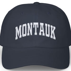 Può includere: Un cappellino da baseball blu navy con la scritta "MONTAUK" in lettere bianche arcuate sul davanti. Il cappellino ha una visiera curva e una corona strutturata, ideale per proteggersi dal sole.