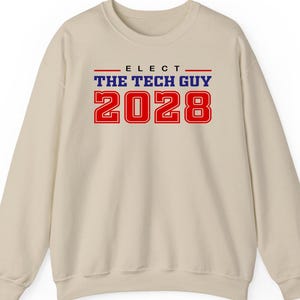 Könnte beinhalten: Beiges Sweatshirt mit dem Text "ELECT THE TECH GUY 2028" in Rot und Blau. Das Sweatshirt hat einen Rundhalsausschnitt und lange Ärmel. Der Text ist mittig auf der Vorderseite platziert.