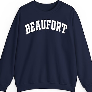 May include: A navy blue sweatshirt with the word "BEAUFORT" printed in large, white, arched letters across the chest. The sweatshirt has a crew neck and long sleeves, suitable for cooler weather.