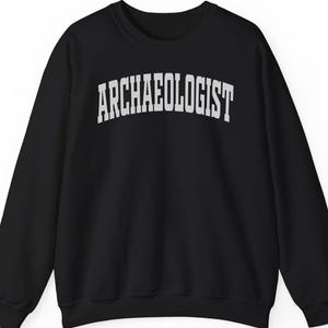 Peut inclure: Sweat-shirt noir à col rond avec le mot "ARCHAEOLOGIST" imprimé en lettres blanches sur la poitrine. Le vêtement à manches longues a une coupe classique et décontractée, convenant à un usage quotidien.