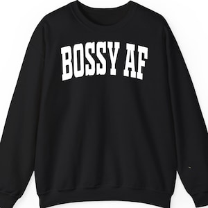 Może przedstawiać: Czarna bluza z okrągłym dekoltem z napisem "BOSS AF" pogrubionymi, białymi literami na piersi. Bluza ma długie rękawy i klasyczny, swobodny krój.