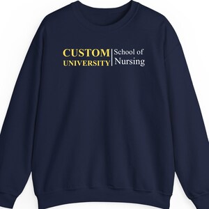 Puede incluir: Sudadera azul marino con el texto "CUSTOM UNIVERSITY School of Nursing" en amarillo y blanco. La sudadera es de cuello redondo y manga larga.