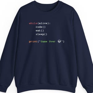 May include: A navy blue sweatshirt with white text that reads "while(alive): code() eat() sleep() print("Game Over" ")". The text is in a programming code format, with the words "Game Over" in orange and a skull icon.