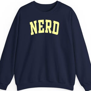 May include: A navy blue sweatshirt featuring the word "NERD" in yellow, block lettering. The crew neck top has long sleeves and is made of a soft material, suitable for casual wear.