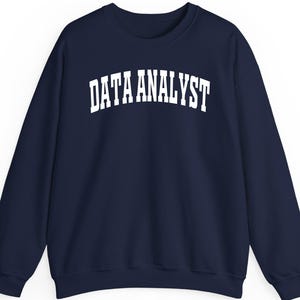 Pode incluir: Camisola azul marinho com a inscrição branca "DATA ANALYST" em letras arqueadas. Esta camisola de gola redonda tem mangas compridas e um corte descontraído. Uma peça casual para profissionais de dados.