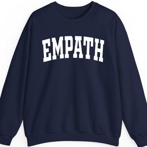 May include: Navy blue sweatshirt with the word "EMPATH" printed in large, white, block letters across the chest. The sweatshirt has a crew neck and long sleeves.
