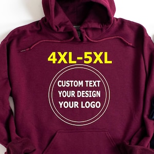 May include: A maroon hoodie with a front pocket and drawstring hood. The text "4XL-5XL" is in yellow at the top, and a white circle with the words "CUSTOM TEXT YOUR DESIGN YOUR LOGO" is in the centre.