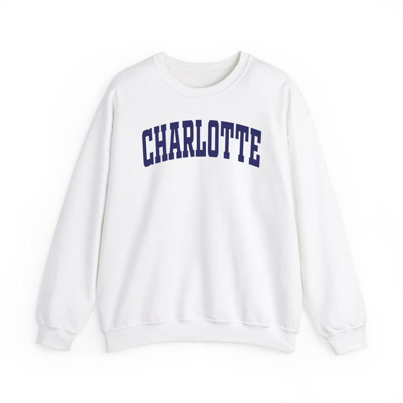 May include: White crew neck sweatshirt with the word "CHARLOTTE" printed in navy blue across the chest. The sweatshirt has long sleeves and a classic, casual design, suitable for everyday wear.
