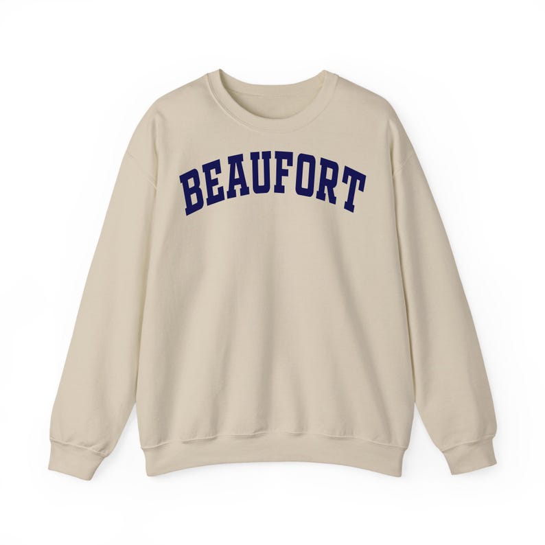 May include: A cream-colored sweatshirt with the word "BEAUFORT" printed across the chest in navy blue, arched lettering. The long-sleeved crewneck top is made of a soft material.