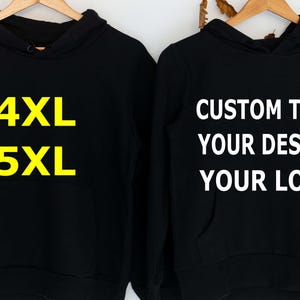 May include: Two black hoodies hanging on wooden hangers. The hoodie on the left has the text "4XL" and "5XL" in yellow. The hoodie on the right has the text "CUSTOM TEXT YOUR DESIGN YOUR LOGO" in white.