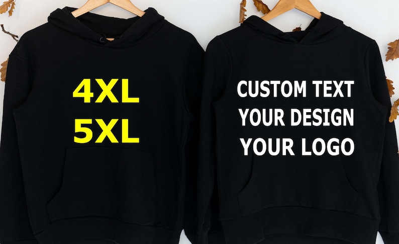 May include: Two black hoodies hanging on wooden hangers. The hoodie on the left has the text "4XL" and "5XL" in yellow. The hoodie on the right has the text "CUSTOM TEXT YOUR DESIGN YOUR LOGO" in white.