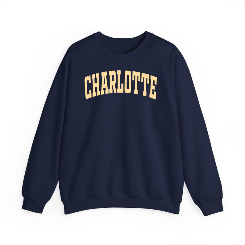 May include: Navy blue crewneck sweatshirt with the word "CHARLOTTE" printed in a gold, collegiate-style font across the chest. The sweatshirt has long sleeves and a classic, casual design.