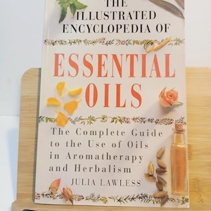 May include: The Illustrated Encyclopedia of Essential Oils book. The cover features the title in orange, with floral and botanical illustrations. The book is a complete guide to the use of oils in aromatherapy and herbalism by Julia Lawless.