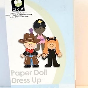 May include: A Cricut Shapes Cartridge box featuring paper doll cutouts. The box has the text "Paper Doll Dress Up" and includes images of a cowboy, a fairy, and a cat. The Cricut logo is visible on the top left.