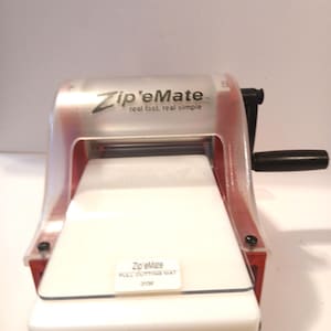 May include: A red and clear plastic Zip'eMate food cutter with a white cutting surface. The device has a black handle and the text "Zip'eMate real fast, real simple" is visible on the top.