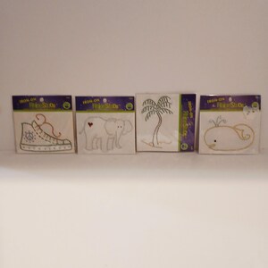May include: Four iron-on fabric stud patches. Designs include a shoe, an elephant with a heart, a palm tree, and a whale. Each patch is on a white background with a black border and the words "IRON-ON Fine Studs".