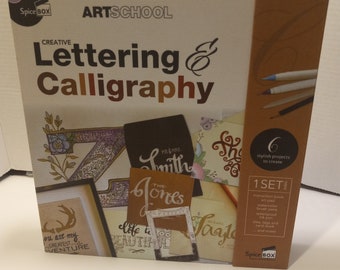 May include: A brown and white box with the title "Artschool Creative Lettering & Calligraphy". The box contains a set of art supplies for creating lettering and calligraphy projects. The box includes an instruction book, art pad, watercolor brush pens, waterproof ink pen, six tags and card stock, and more.