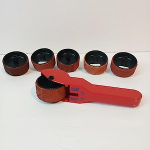 May include: A red hand-held sanding tool with a sanding drum attached, and five additional sanding drums. The drums are brown with black centers. The tool is designed for woodworking and other DIY projects.