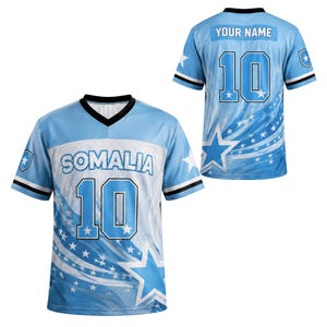 May include: A light blue V-neck jersey featuring the word SOMALIA and the number 10 on the front. The back displays the text YOUR NAME above the number 10. The design includes white star patterns, black trim on the collar and sleeves, and a mesh panel.