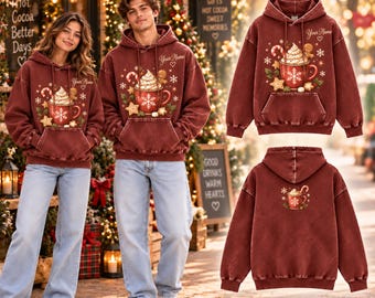 May include: A maroon mineral-washed hoodie featuring a front graphic of a mug filled with whipped cream, a candy cane, and gingerbread cookies. The text "Your Name" is printed above the mug. The back of the hoodie displays a smaller version of the same mug graphic.