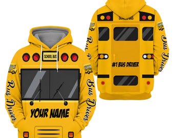 May include: A yellow hoodie featuring a school bus graphic. The front displays a windscreen, wipers, and the text 'YOUR NAME'. The back shows a bus door with the text '#1 BUS DRIVER'. Both sleeves feature the text 'Bus Driver' in script.