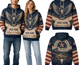 May include: A navy blue hooded sweatshirt featuring a graphic of a bald eagle with spread wings, stars, and stripes. The front pocket area displays the text YOUR NAME. The back features a landscape with a star, mountains, and a steer skull.