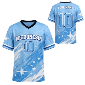 May include: A light blue V-neck jersey featuring the text MICRONESIA and the number 10 on the front, with a matching back view showing the text YOUR NAME and the number 10. The design includes white star graphics, blue brush strokes, and sleeve patches.