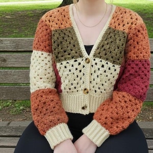 May include: A colorful, crocheted cardigan in a patchwork design. The sweater features a V-neck and button closure. The color palette includes cream, orange, brown, and burgundy. The sleeves and bottom hem are cream-colored.