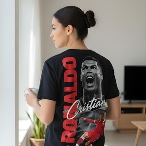 May include: Black t-shirt featuring a large image of Cristiano Ronaldo with the name "Ronaldo" in red block letters and "Cristian" in white script. The shirt also has an image of Ronaldo in a soccer uniform.