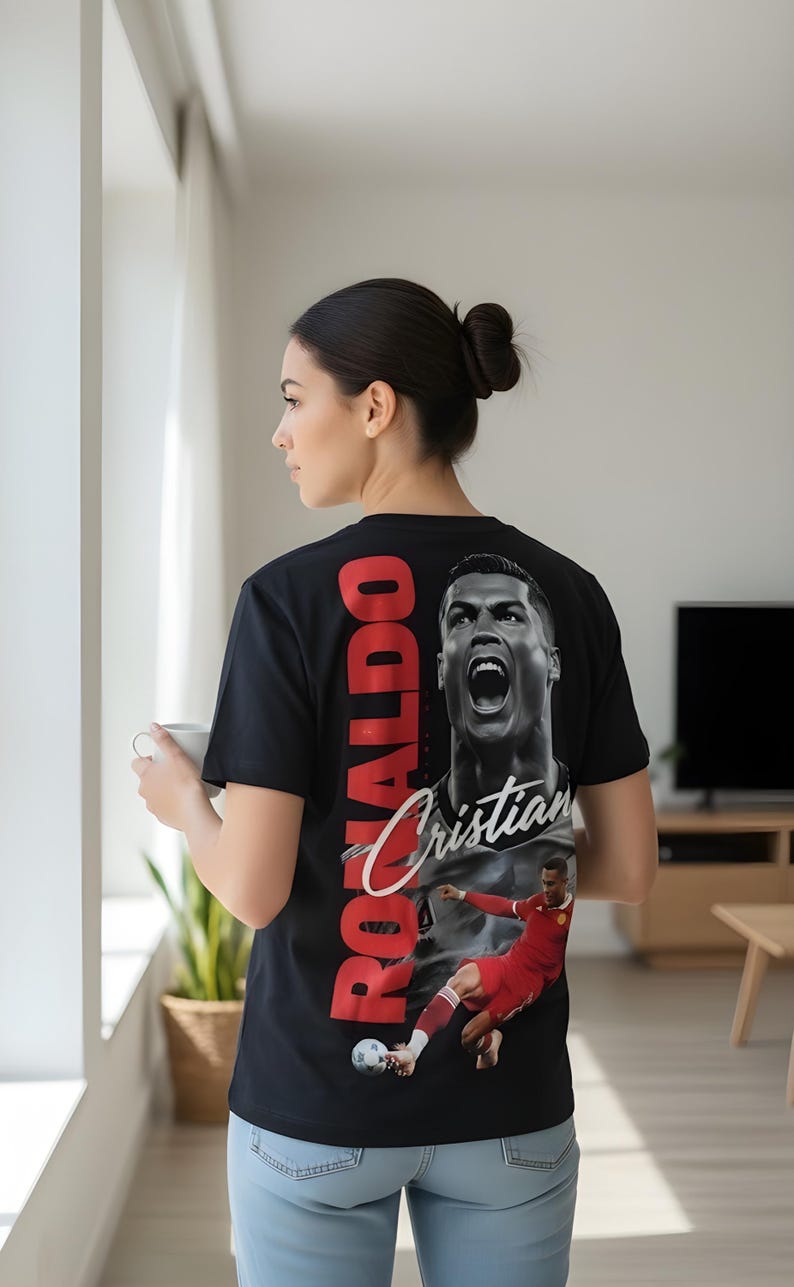 May include: Black t-shirt featuring a large image of Cristiano Ronaldo with the name "Ronaldo" in red block letters and "Cristian" in white script. The shirt also has an image of Ronaldo in a soccer uniform.