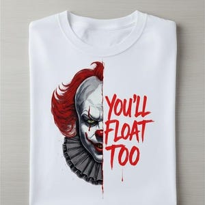 May include: White t-shirt featuring a half-face image of a scary clown with red hair and makeup. The text "You'll Float Too" is printed in red on the right side of the shirt. The shirt is folded.