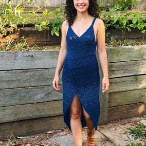 Puede incluir: Vestido de crochet azul marino con cuello en V y abertura frontal. El vestido tiene un corpiño ajustado y una falda fluida. La persona lleva sandalias marrones. Estilo de verano o playa.