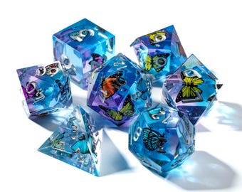May include: A set of seven polyhedral dice with a butterfly theme. The dice are clear with blue and purple hues, and each die features a different butterfly design. The numbers are silver. The dice are for tabletop games.