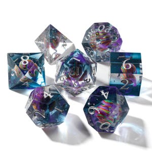 May include: A set of seven polyhedral dice for tabletop games. Each die is clear with a swirling, colorful design inside, featuring shades of purple, blue, and red. The numbers are silver. The dice are arranged on a white surface.