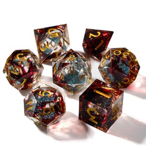 May include: Set of seven polyhedral dice with a red and gold color scheme. The dice are transparent with red and gold inclusions, and gold numbering. The dice are designed for tabletop role-playing games.