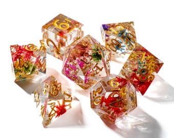 May include: A set of seven clear resin dice with embedded colorful flowers and gold numbering. The dice are in various geometric shapes, including a cube, a d20, and a d6, perfect for tabletop gaming.