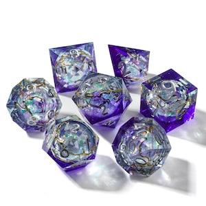 May include: Set of seven polyhedral dice with a purple and iridescent design. Each die has silver numbering and gold-colored accents. The dice are made of a clear resin with a glittery, celestial appearance.