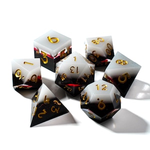 Puede incluir: Un conjunto de siete dados poliédricos con un diseño degradado blanco y negro. Los dados tienen números dorados y están hechos de un material de resina transparente. El conjunto incluye un D4, D6, D8, D10, D12, D20 y un dado de porcentaje.