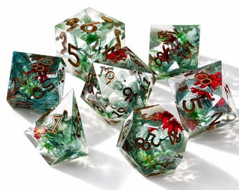 May include: A set of seven polyhedral dice made of clear resin, each containing embedded green skeletonized leaves and small red flowers. The dice feature metallic copper-colored numbers etched into the surfaces, showcasing various geometric shapes including cubes, pyramids, and multi-faceted polyhedrons.