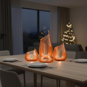May include: A dining table set with four copper-colored, abstract candle holders. The candle holders have a vertical, slatted design. The table is set with plates, silverware, and placemats. A Christmas tree is visible in the background.
