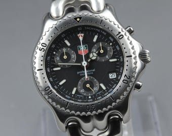 May include: A stainless steel TAG Heuer professional wristwatch with a black dial. The watch features a tachymeter bezel, chronograph subdials, and a date display. The watch is water resistant to 200 meters.