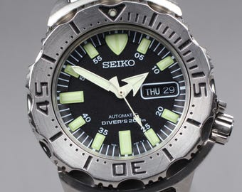 May include: A stainless steel Seiko automatic diver's watch with a black dial. The watch features luminous hands and markers, a date display, and a rotating bezel. The watch is water resistant to 200 meters.