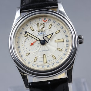 May include: A silver Oris automatic wristwatch with a cream face and black leather strap. The watch face has black hands, a red second hand, and a date display. The watch is marked '27 jewels'.