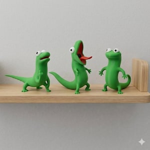 May include: Three green lizard figurines with expressive faces are displayed on a wooden shelf. One lizard has its mouth open, revealing a red tongue. The other two lizards have different poses, adding a playful touch to the decor.