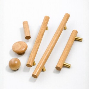 May include: A collection of wooden cabinet hardware, including cylindrical pulls and knobs. The hardware is made of light-colored wood with brass-colored accents. The pulls are approximately 6 inches long.