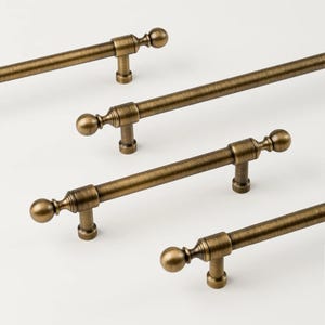 May include: Four antique brass cabinet pulls with a ball-shaped end and a decorative base. The pulls are arranged diagonally against a white background. The hardware has a vintage aesthetic.