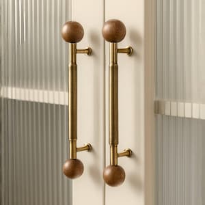 May include: Two cabinet door pulls with a wooden ball at each end. The pulls have a brass finish with a textured center section. The cabinet doors are off-white with a ribbed glass panel.