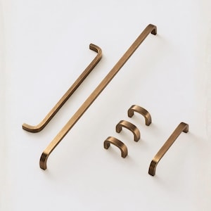 Peut inclure: Ensemble de quincaillerie de meubles en bronze, comprenant des poignées de barres et des poignées incurvées de différentes tailles. L'ensemble est présenté sur un fond blanc, mettant en valeur les différents modèles.